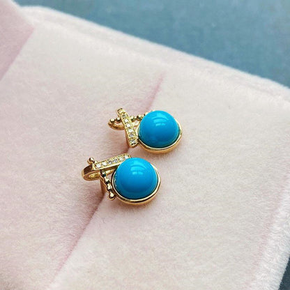 Turquoise earrings with gold accents on a soft pink surface